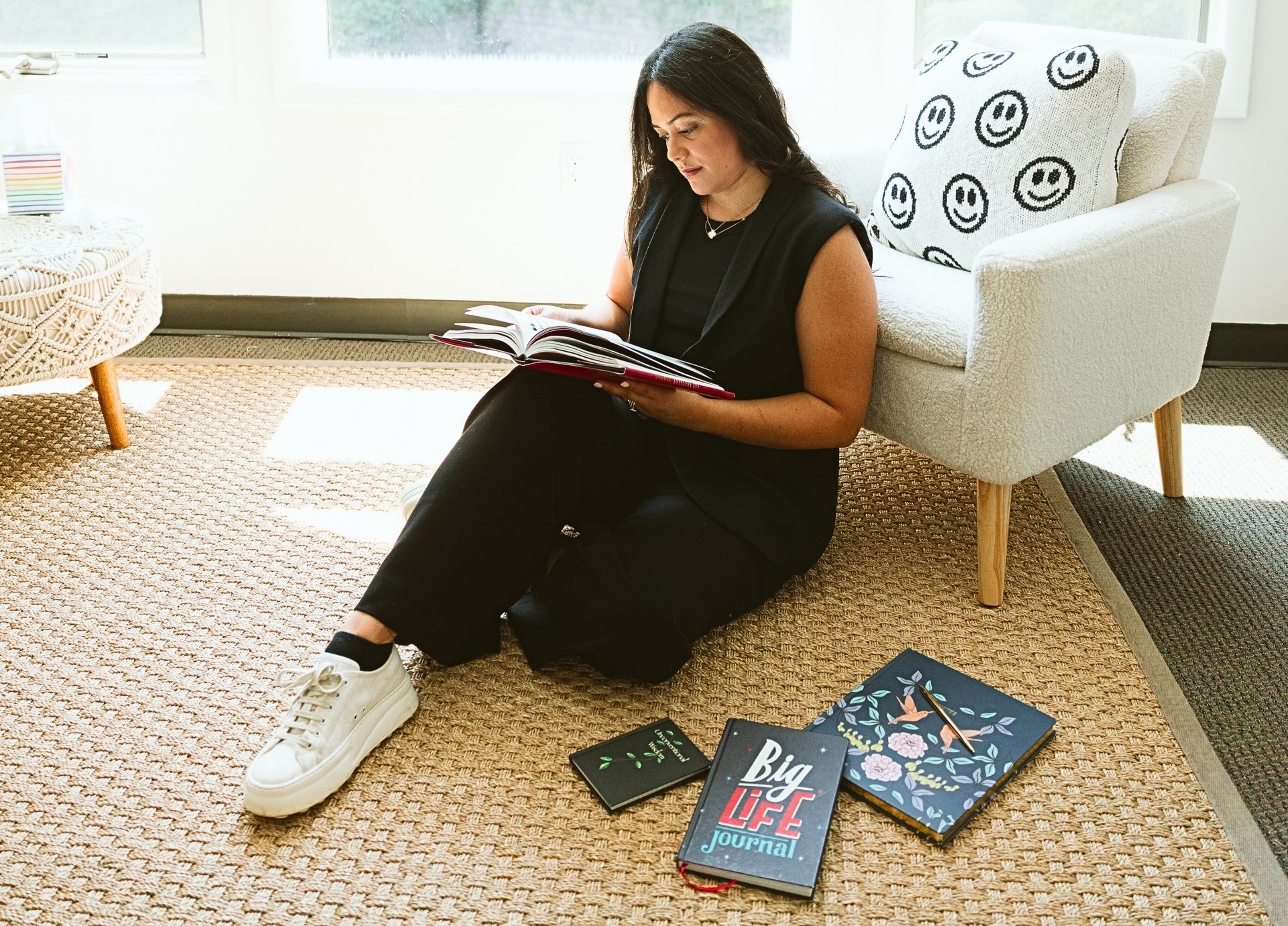 Erika Valencia sitting on the floor reading a journal in a cozy therapy space surrounded by self-help and mindfulness books