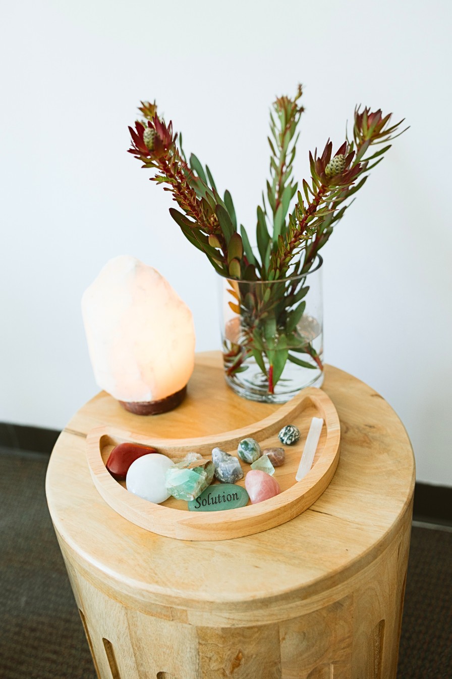 A peaceful therapy corner featuring healing crystals, a glowing Himalayan salt lamp, and fresh greenery on a wooden table at Mindfully Life